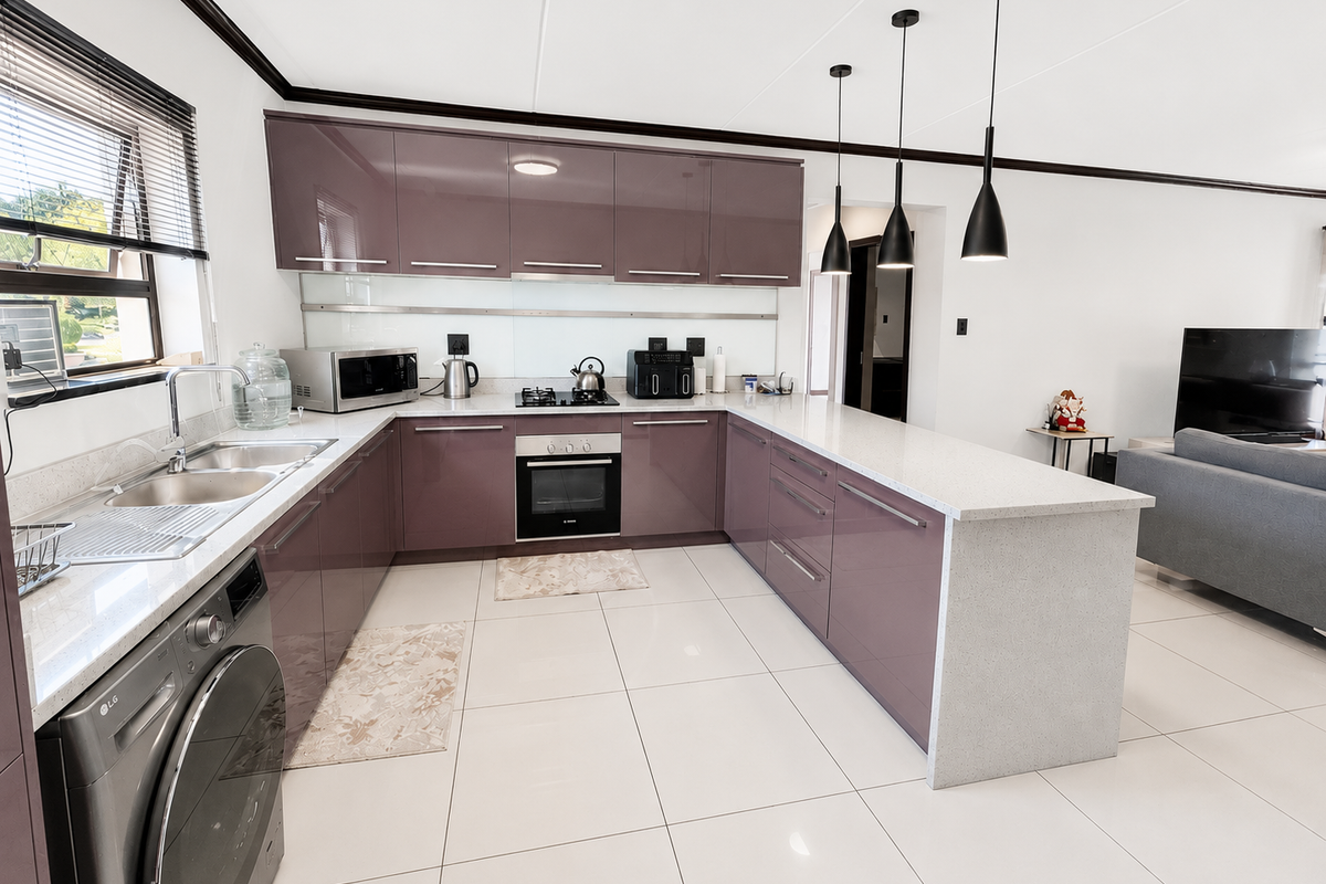 Modern open-plan kitchen featuring high-gloss purple cabinetry, stone countertops, integrated appliances, and sleek pendant lighting, seamlessly flowing into the adjacent living area.