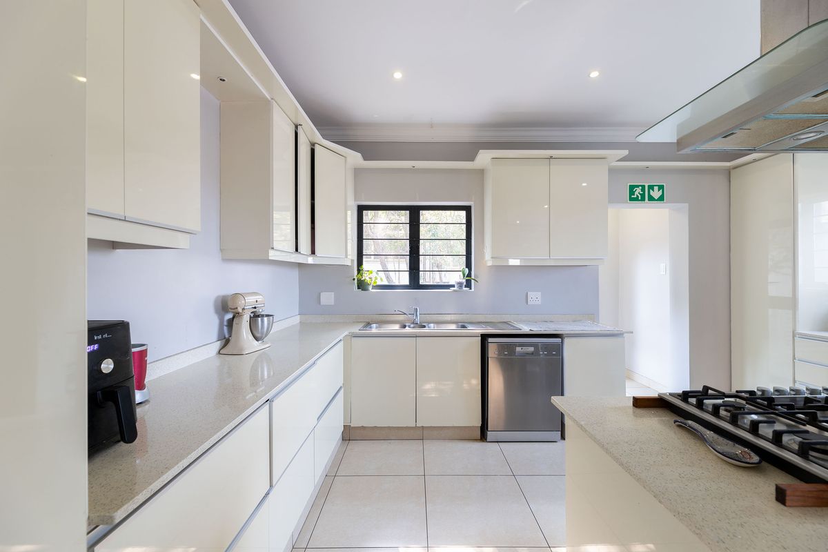 Modern kitchen featuring high-gloss cabinetry, stone countertops, a gas hob with extractor fan, and tiled flooring.