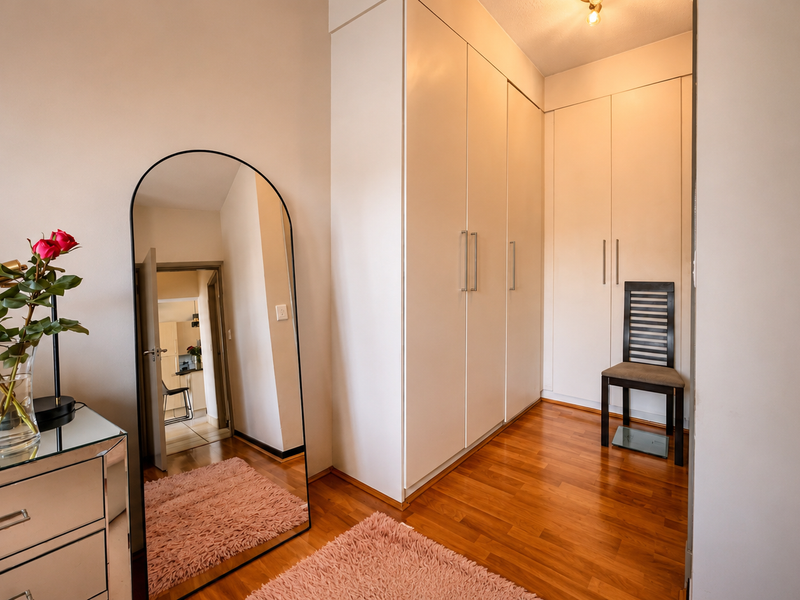 A well-maintained bedroom featuring light-toned built-in cupboards and warm laminate flooring, offering ample storage space.