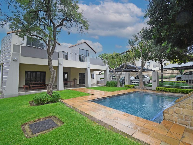 Rear view of the apartment featuring a private swimming pool, stone-paved pool deck, covered patio, upper-level balcony, and a well-maintained garden area.