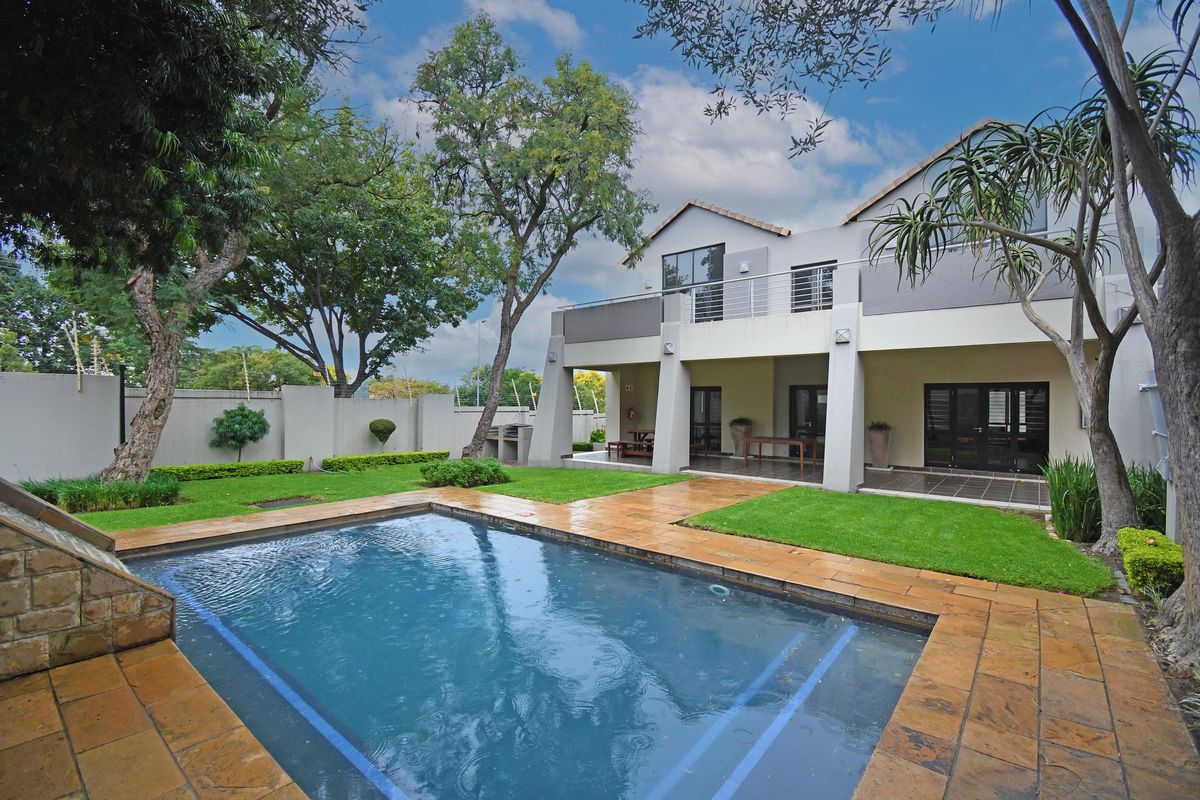 Rear view of a two-story apartment featuring a swimming pool, stone-paved patio, landscaped garden, and an upper-level balcony.