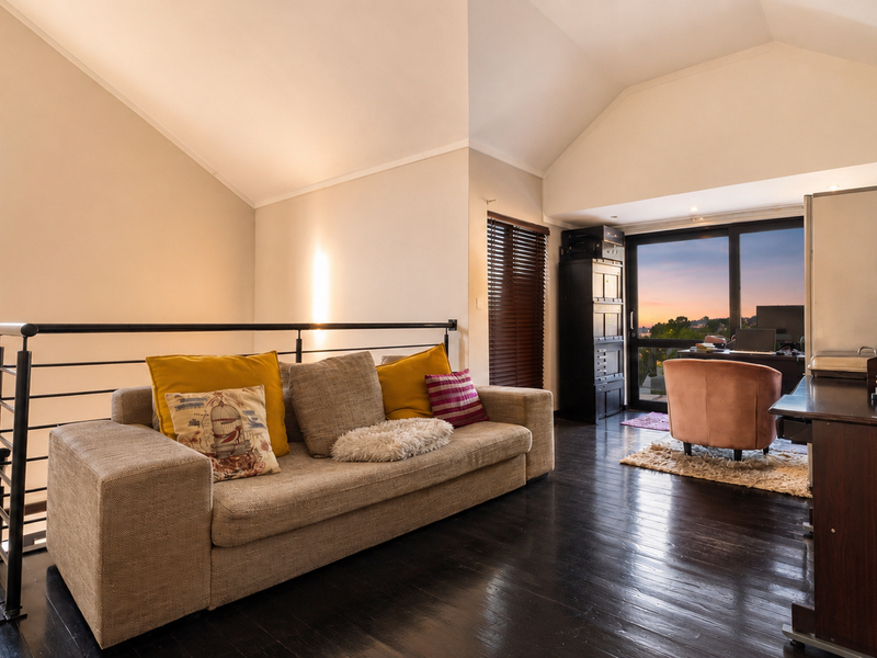 A spacious living area featuring vaulted ceilings, dark timber flooring, and a metal balustrade, with large sliding doors providing access to an outdoor view.