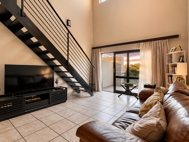 Spacious double-volume living room featuring a modern metal staircase, tiled flooring, and large sliding glass doors leading to an outdoor balcony area.