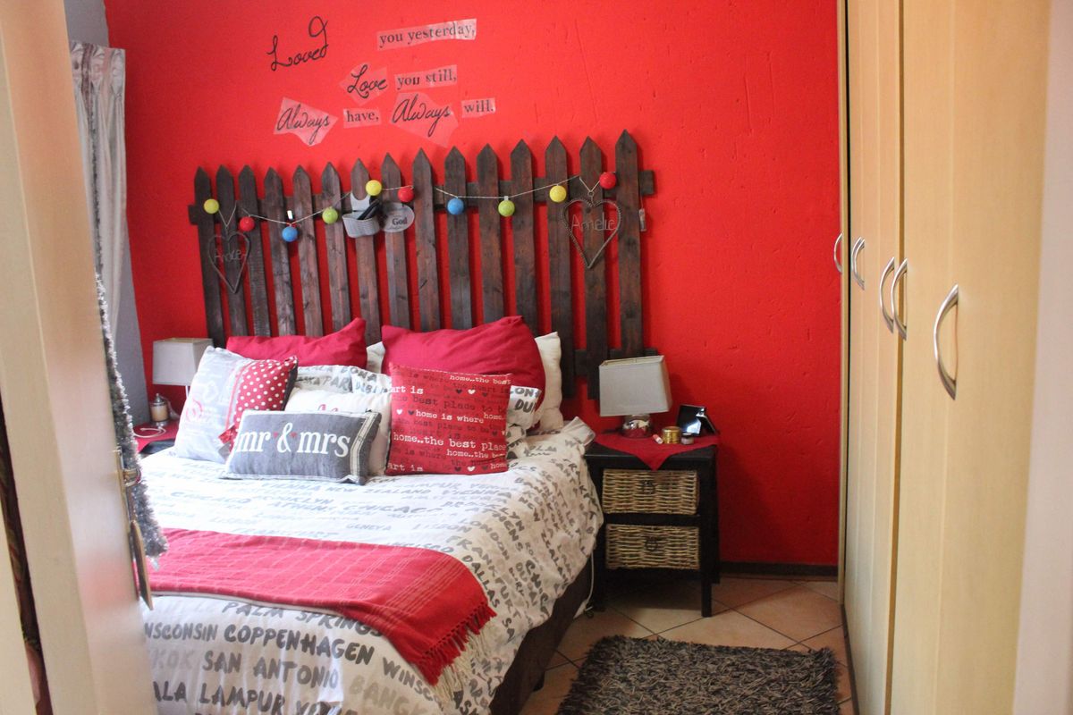 A bedroom featuring built-in cupboards and tiled flooring, currently styled with a bold red accent wall.
