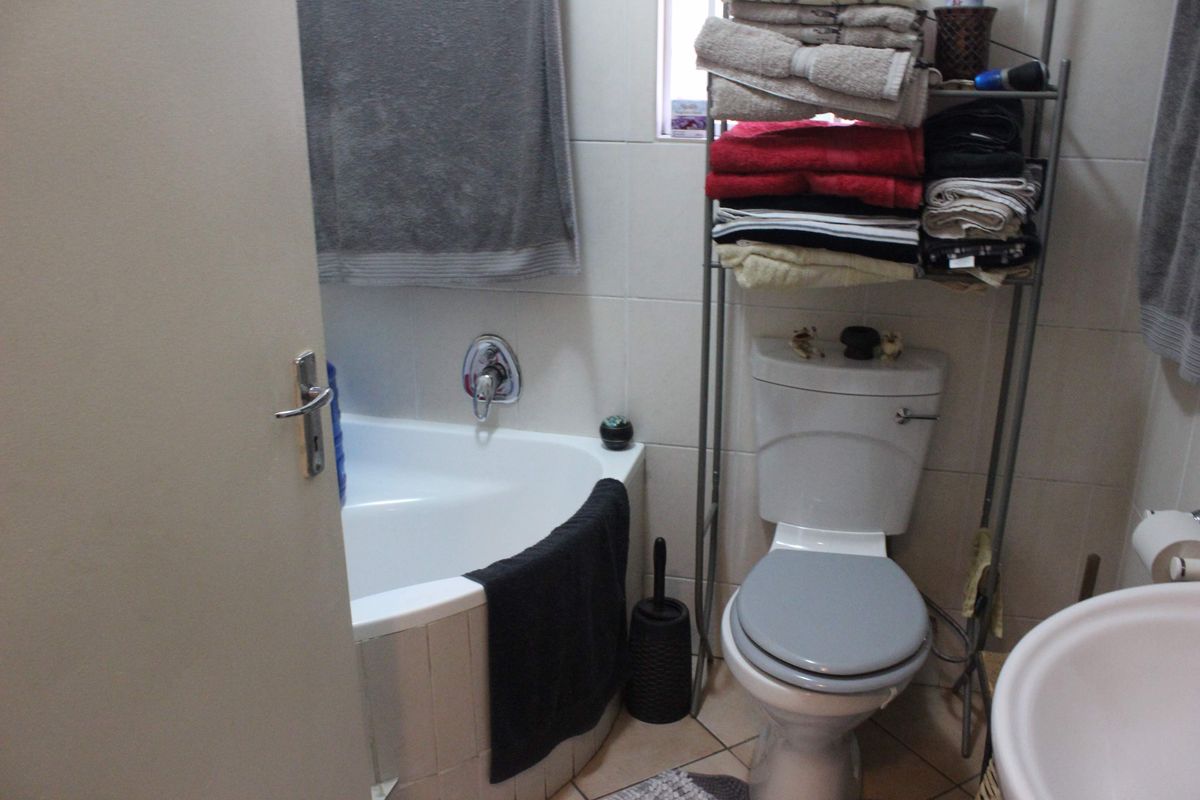 A compact bathroom featuring a corner bathtub, a standard toilet, and a pedestal basin with tiled finishes throughout.