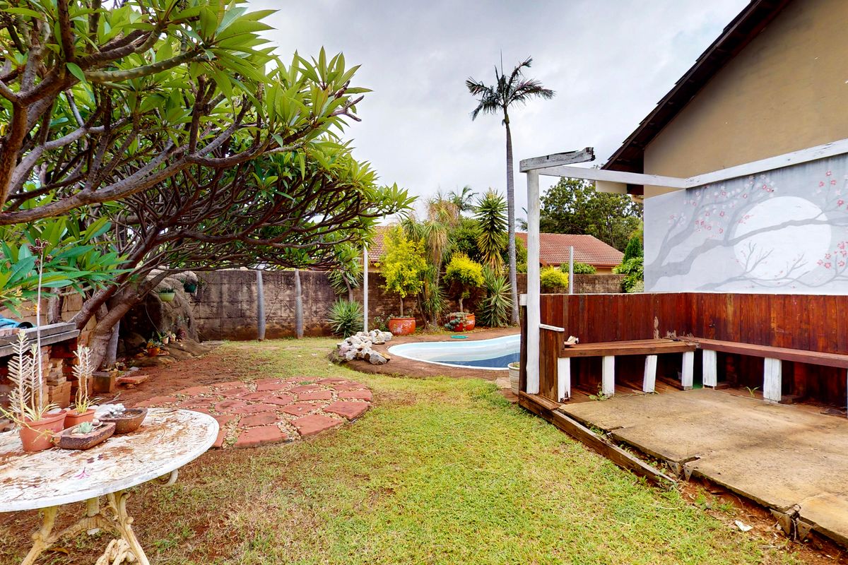 Rear garden area featuring a swimming pool, a built-in wooden bench on a concrete patio, and established landscaping with mature trees.