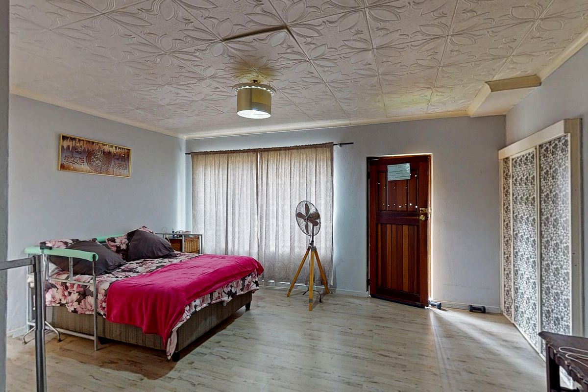 A spacious bedroom featuring light wood-look flooring, a textured ceiling, and a built-in wardrobe with decorative paneling.