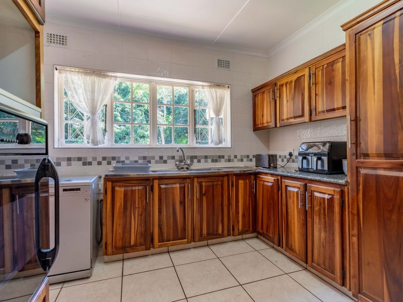 A functional kitchen featuring warm-toned wooden cabinetry, tiled backsplash, ample counter space, and a large window providing natural light.