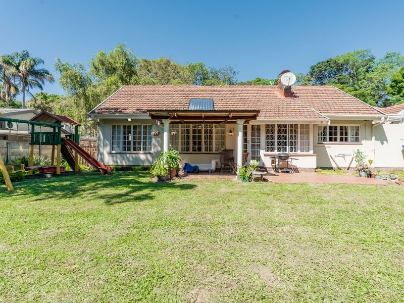 Rear view of the house featuring a covered patio with a timber pergola, terracotta tiled roof, and a spacious garden area.