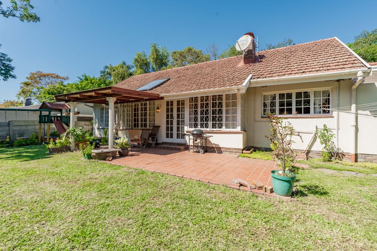 Rear view of the house featuring a terracotta tiled patio, covered pergola, and established garden area with classic lattice window detailing.