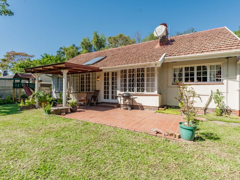 Rear view of the house featuring a terracotta tiled patio, covered pergola, and established garden area with classic lattice window detailing.