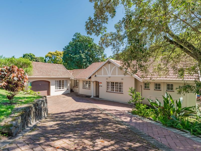 Front elevation of a well-maintained house featuring a tiled roof, brick driveway, and an integrated garage, set within a landscaped garden.