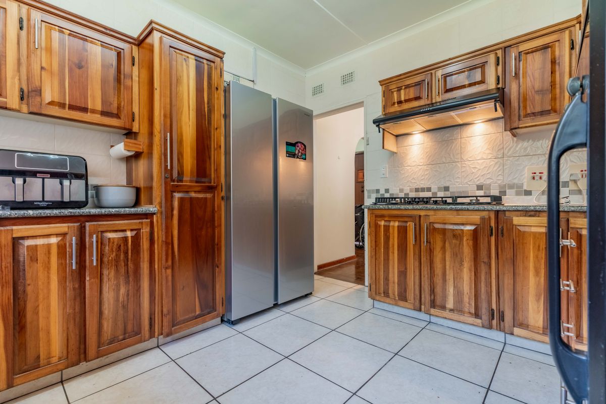 A functional kitchen featuring warm-toned wooden cabinetry, granite countertops, a gas hob with extractor fan, and neutral tiled flooring.