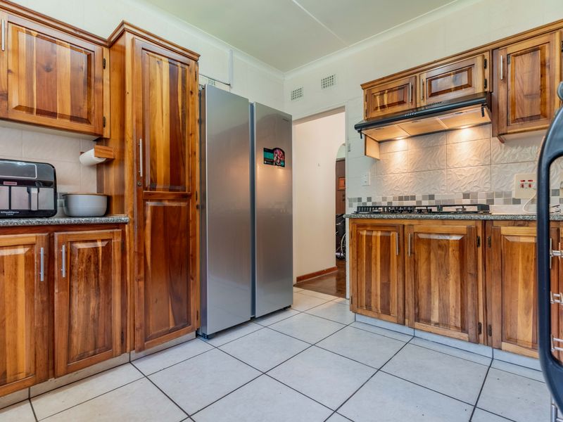 A functional kitchen featuring warm-toned wooden cabinetry, granite countertops, a gas hob with extractor fan, and neutral tiled flooring.