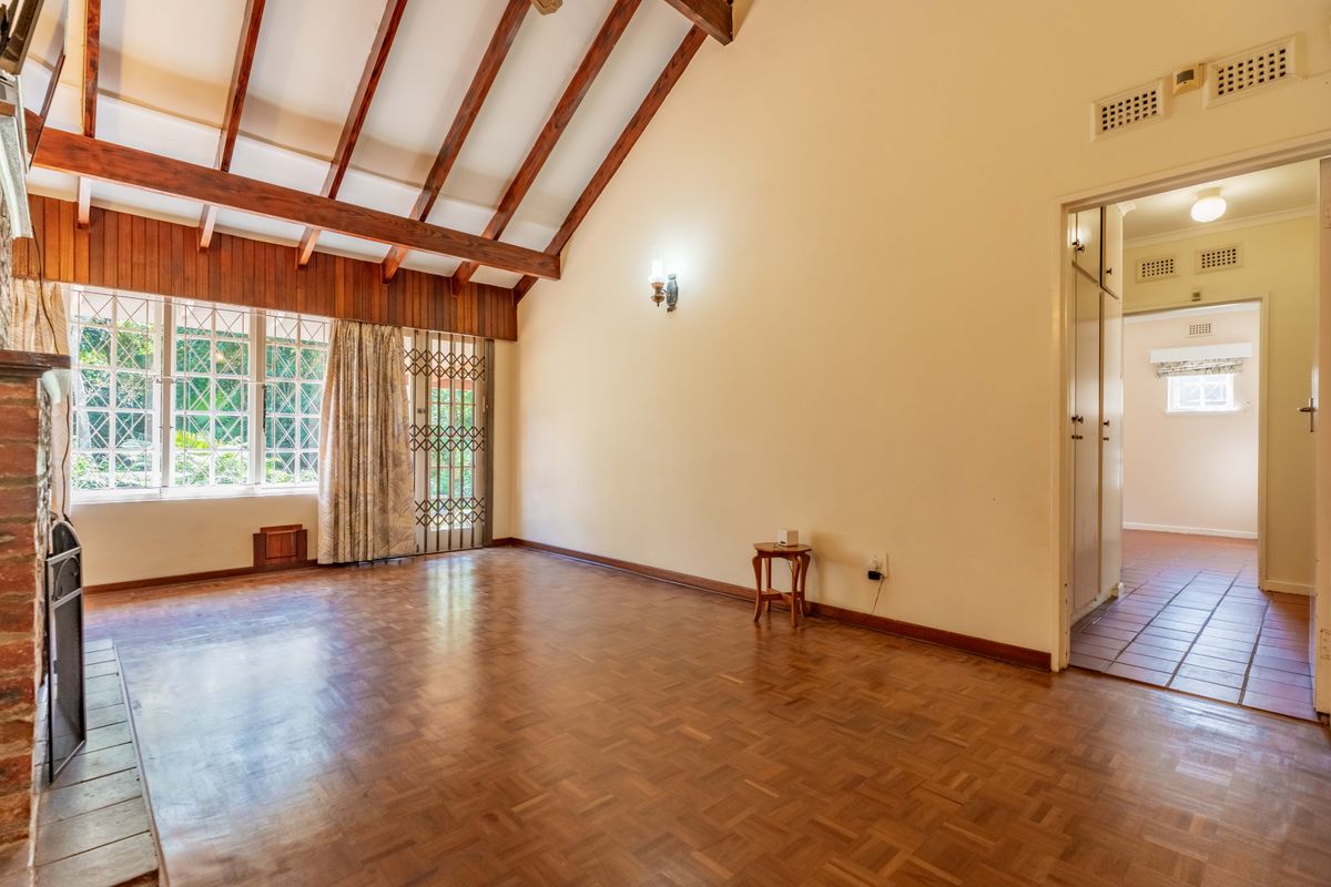 Spacious living room featuring high vaulted ceilings with exposed timber beams, classic parquet flooring, and a brick fireplace, offering a bright and open atmosphere.