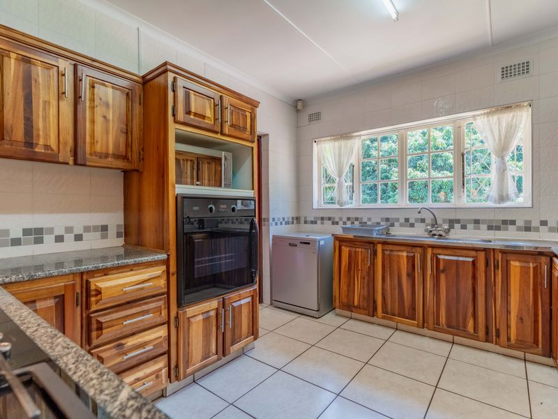 A functional kitchen featuring warm wooden cabinetry, granite countertops, a built-in oven, gas hob, and tiled flooring with ample natural light.