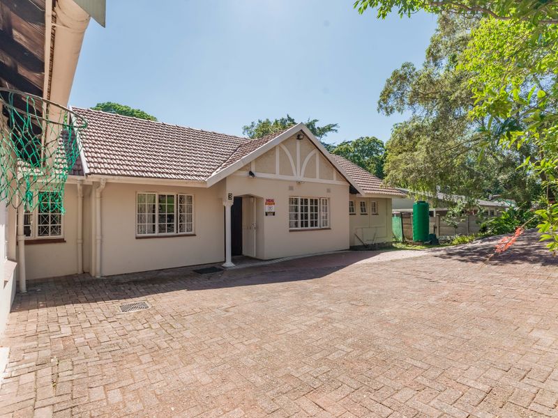 Front exterior view of the house featuring a paved driveway, tiled roof, and established garden surroundings.