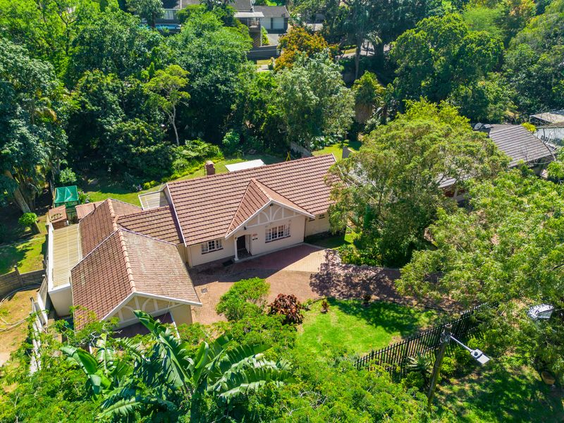 Aerial view of a residential property featuring a tiled roof, brick driveway, and established garden surroundings.