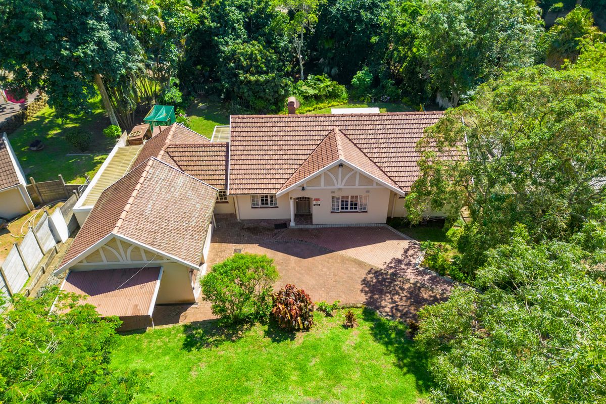 Aerial view of a residential property featuring a tiled roof, brick driveway, and established garden surroundings.