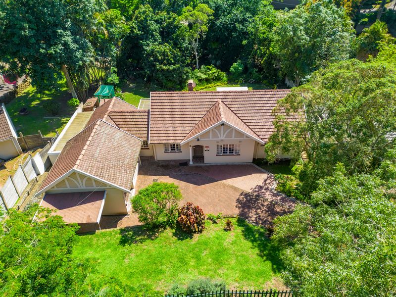 Aerial view of a residential property featuring a tiled roof, brick driveway, and established garden surroundings.