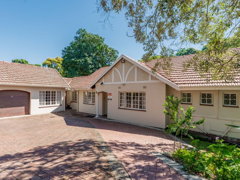 Front elevation of a well-maintained house featuring a tiled roof, gabled architecture, and a spacious brick-paved driveway leading to a garage.
