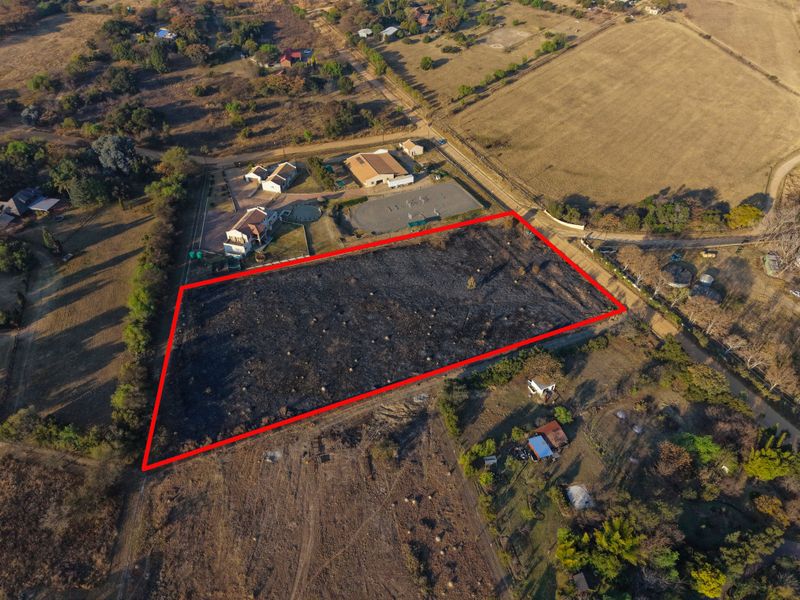 An aerial view of a vacant residential plot of land, clearly outlined in red, situated within a rural or semi-rural landscape.