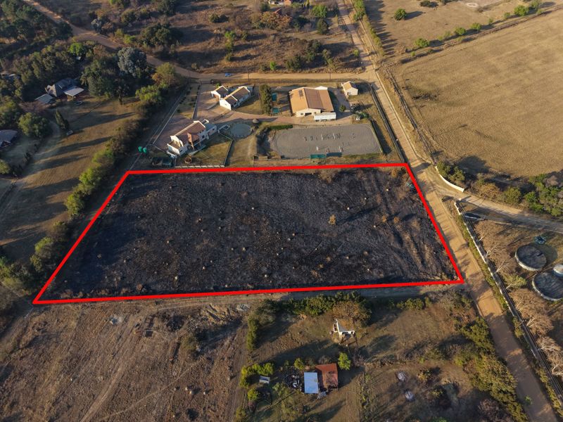 An aerial view of a vacant residential plot of land, clearly outlined in red, situated within a rural estate setting.