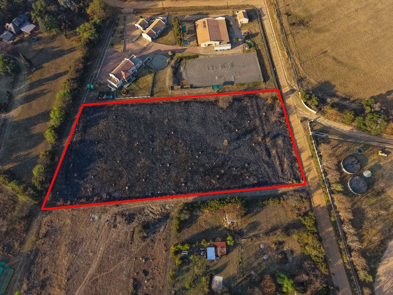 Aerial view of a vacant residential plot with clear boundary markings, showing cleared land with signs of recent vegetation burning.