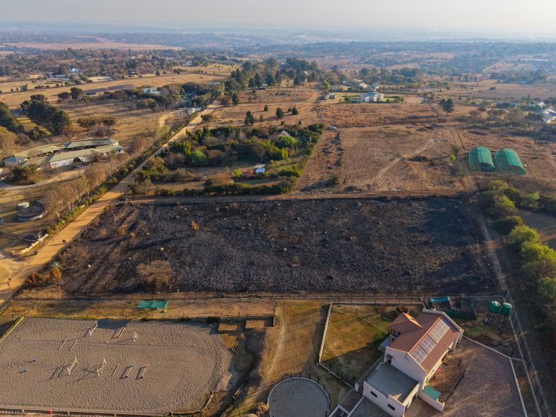 Aerial view of a residential plot featuring a cleared, scorched land area, adjacent equestrian facilities, and a main dwelling with solar panels.