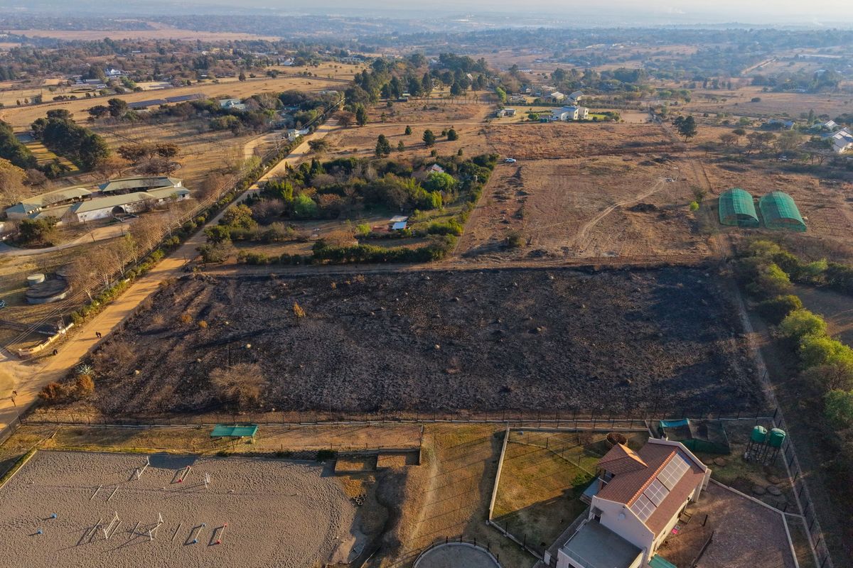 Aerial view of a residential plot featuring a cleared, scorched land area, adjacent equestrian facilities, and a main dwelling with solar panels.