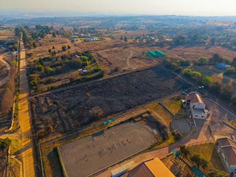Aerial view of a residential property featuring an equestrian arena, round pen, and fenced land in a rural setting.