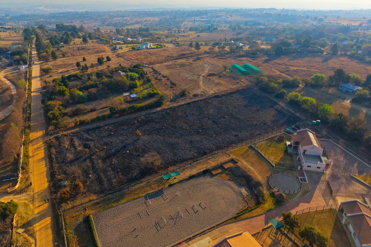 Aerial view of a residential property featuring an equestrian arena, round pen, and fenced land in a rural setting.
