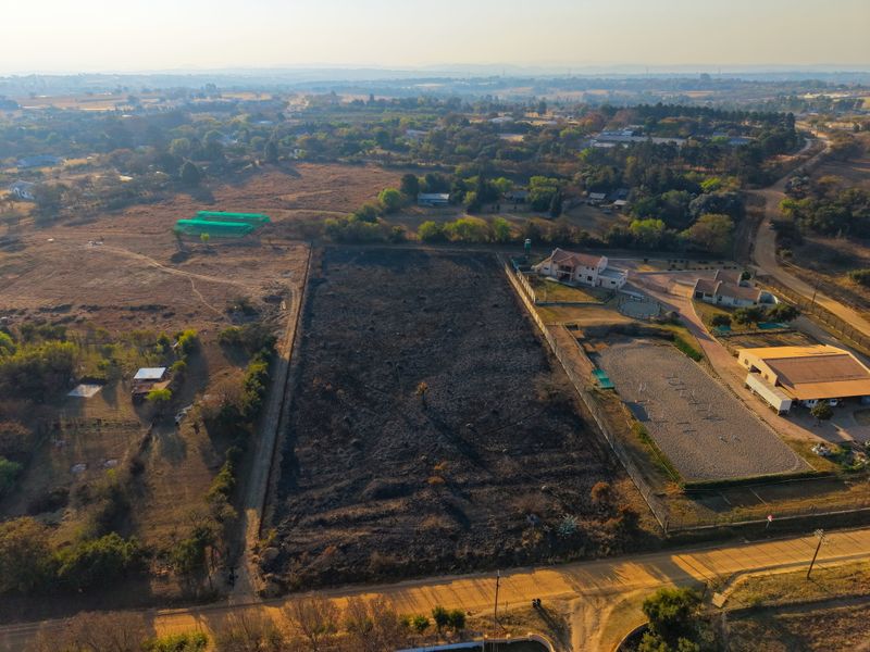 Aerial view of a vacant residential plot featuring open land with perimeter fencing and direct access to a dirt road.