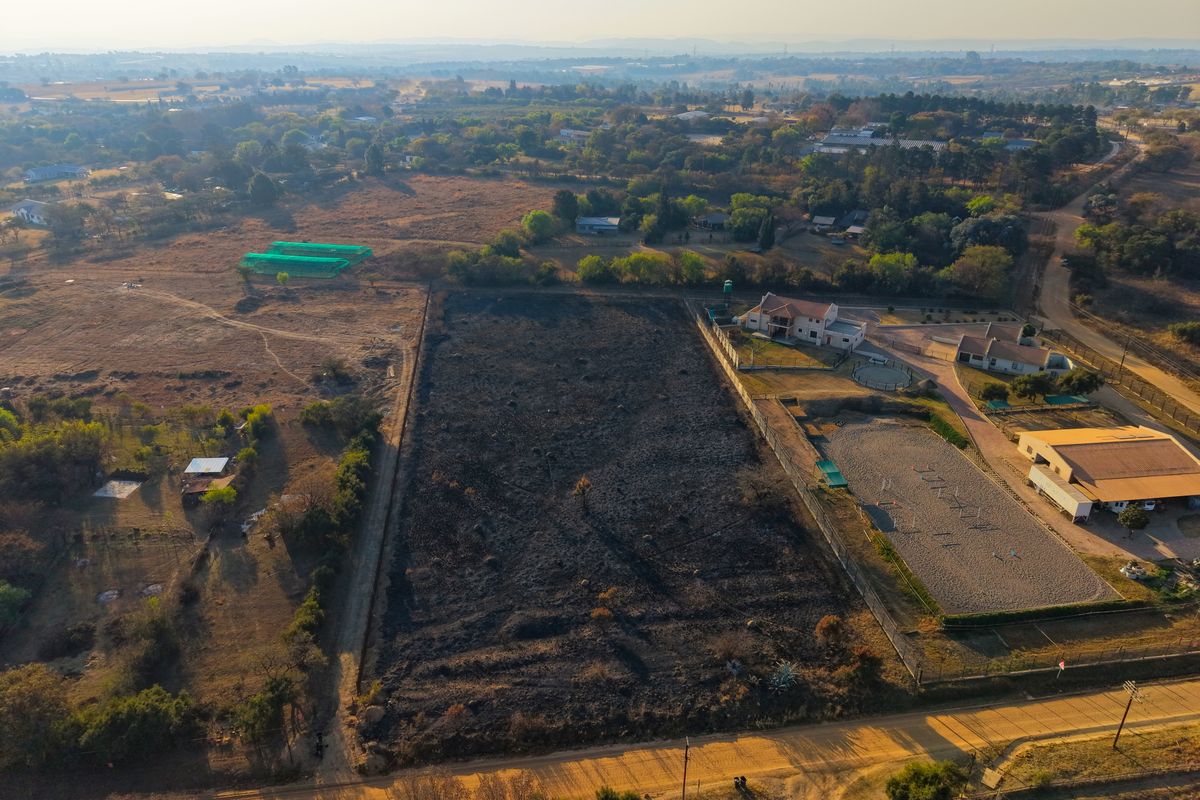 Aerial view of a vacant residential plot featuring open land with perimeter fencing and direct access to a dirt road.