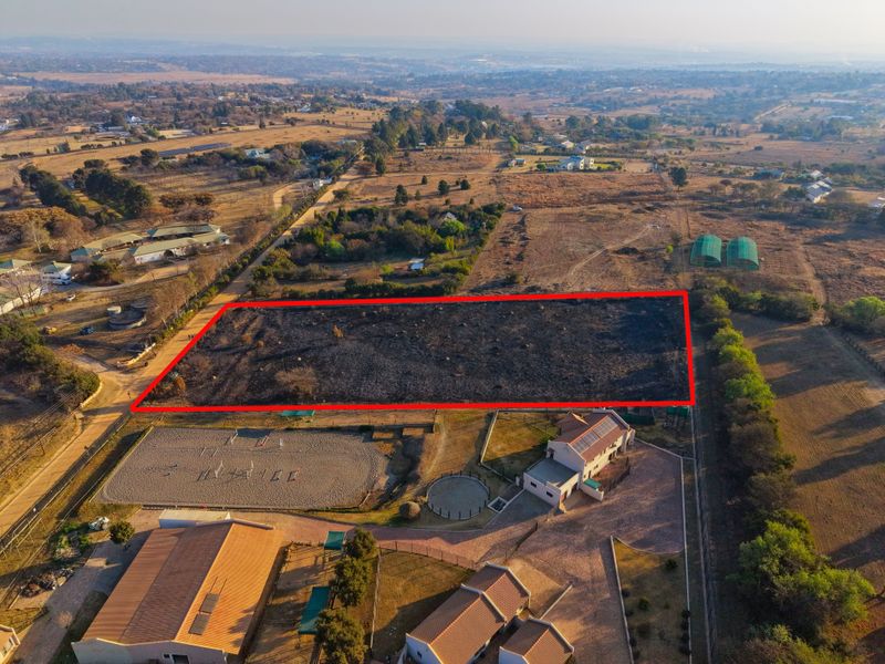 Aerial view of a vacant residential plot outlined in red, situated within a rural estate setting with surrounding infrastructure.