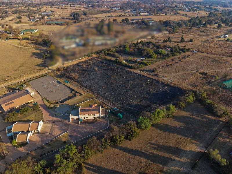 Aerial view of a residential property featuring a main dwelling with solar panels, a paved driveway, and an equestrian arena on a large plot.