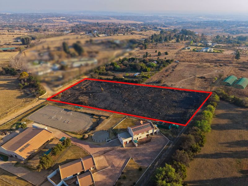 Aerial view of a vacant residential plot marked with a red boundary, situated in a rural estate setting.
