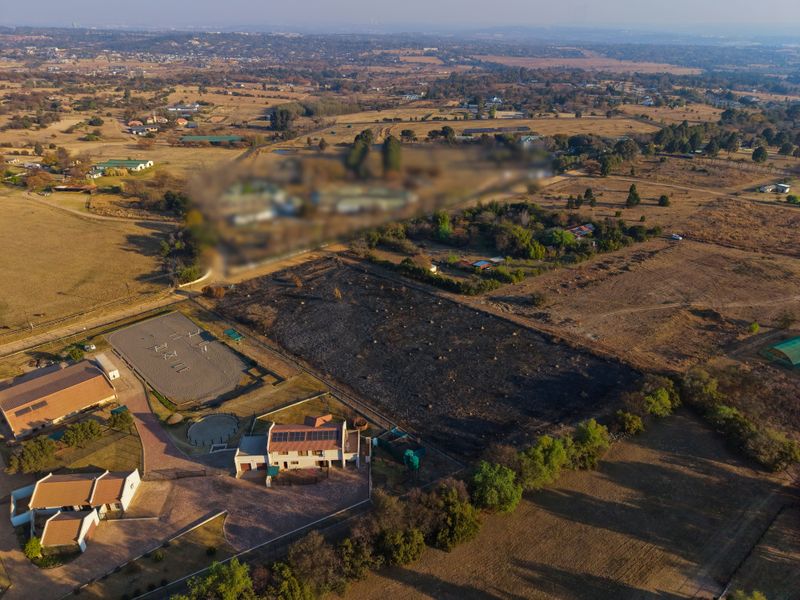 Aerial view of a residential property featuring a main dwelling with solar panels, a paved driveway, and an adjacent riding arena on a large plot.