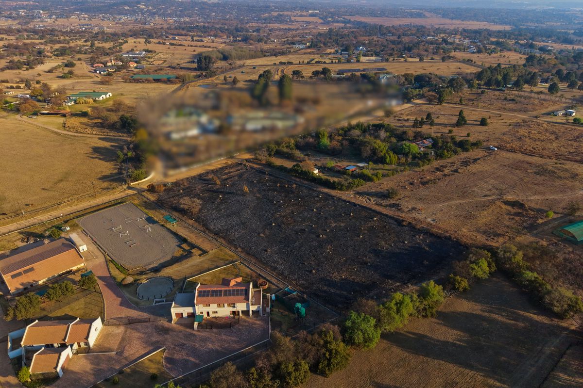 Aerial view of a residential property featuring a main dwelling with solar panels, a paved driveway, and an adjacent riding arena on a large plot.