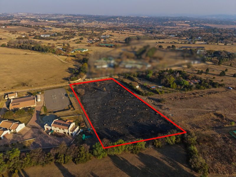 Aerial view of a vacant residential plot outlined in red, situated in a semi-rural landscape with surrounding properties.