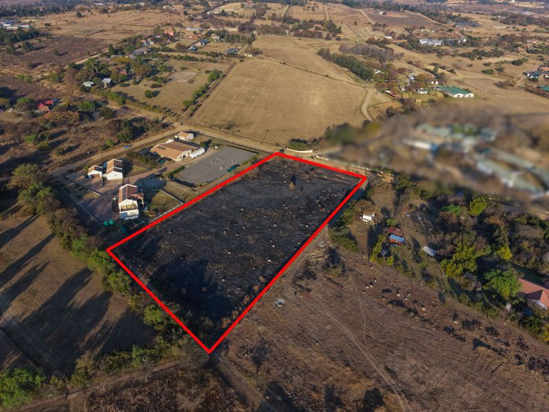 Aerial view of a vacant residential plot outlined in red, situated in a rural estate setting with surrounding vegetation.