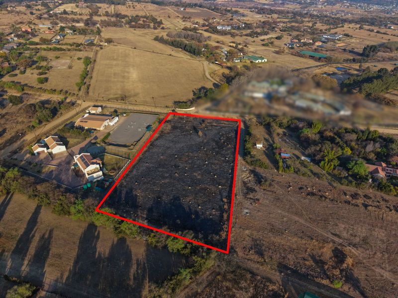 Aerial view of a vacant residential plot with red boundary lines indicating the property perimeter in a rural setting.