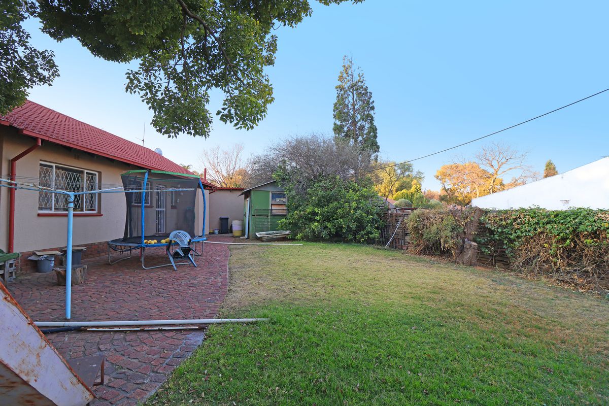 A rear exterior view of the property featuring a paved patio area, a lawned garden, and a small storage shed.