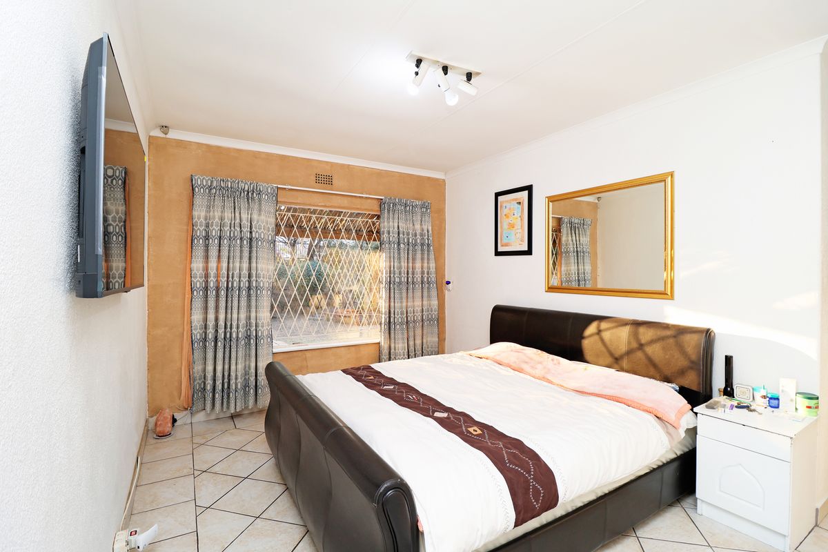 A bedroom featuring tiled flooring, a window with security bars, and a ceiling-mounted light fixture.