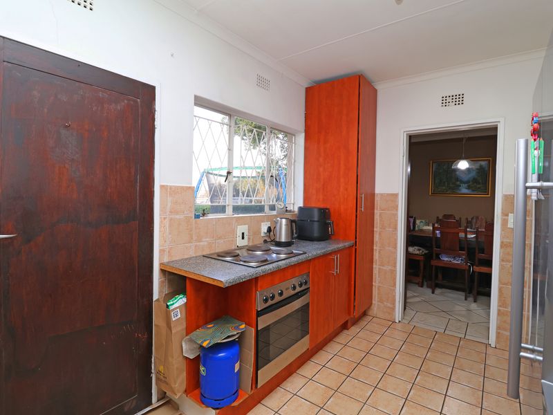 A functional kitchen featuring wood-finish cabinetry, a built-in oven and hob, tiled backsplash, and tiled flooring, with direct access to the dining area.