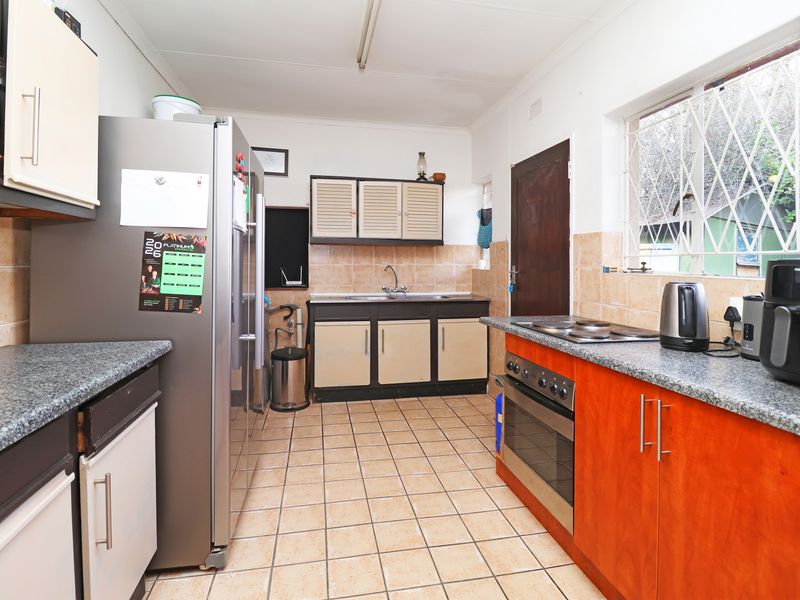 Functional kitchen featuring granite countertops, built-in cabinetry, stainless steel oven, electric hob, and tiled flooring with a practical layout.