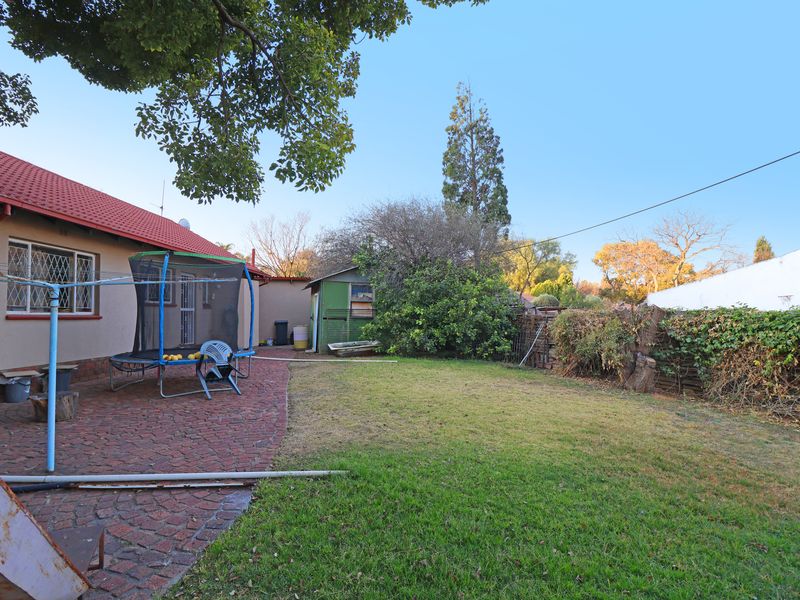 A rear exterior view of the property featuring a paved patio area, a lawned garden, and a small storage shed.