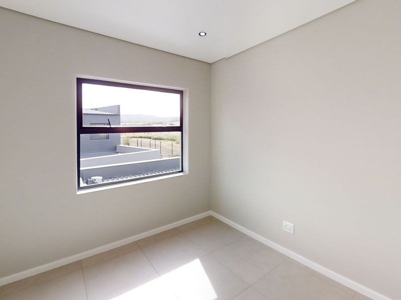 A bright, empty bedroom featuring neutral wall finishes, tiled flooring, and a modern aluminium-framed window with views of the surrounding estate.