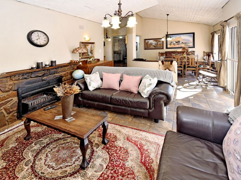 Spacious open-plan living and dining area featuring a prominent stone fireplace, tiled flooring, and vaulted ceilings with exposed beams.