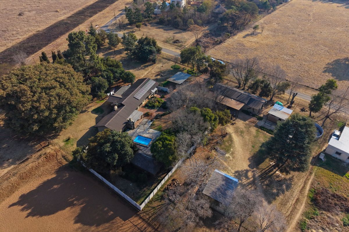 Aerial view of a large rural property featuring a main residence with solar panels, a swimming pool, and multiple outbuildings on a spacious plot.